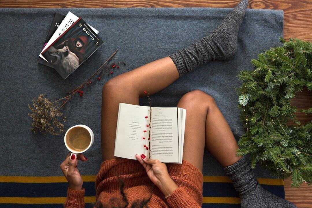 opened book on person&#39;s lap with gray socks