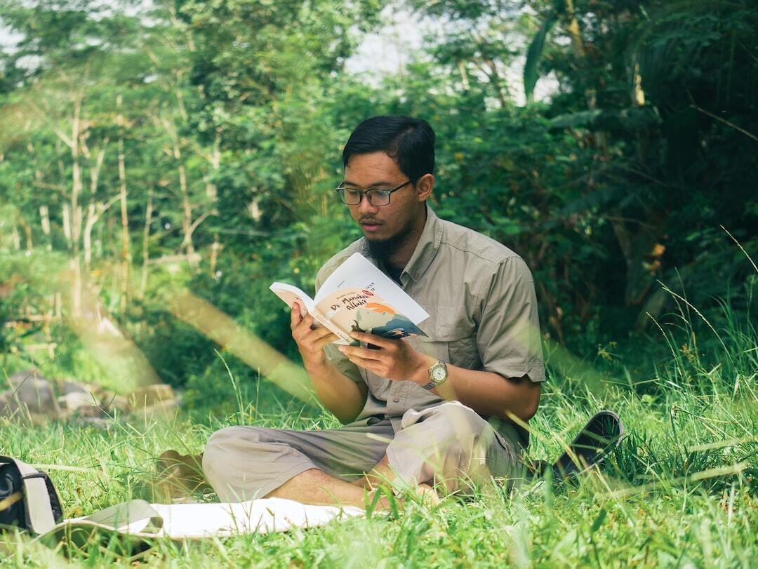 a man sitting in the grass reading a book